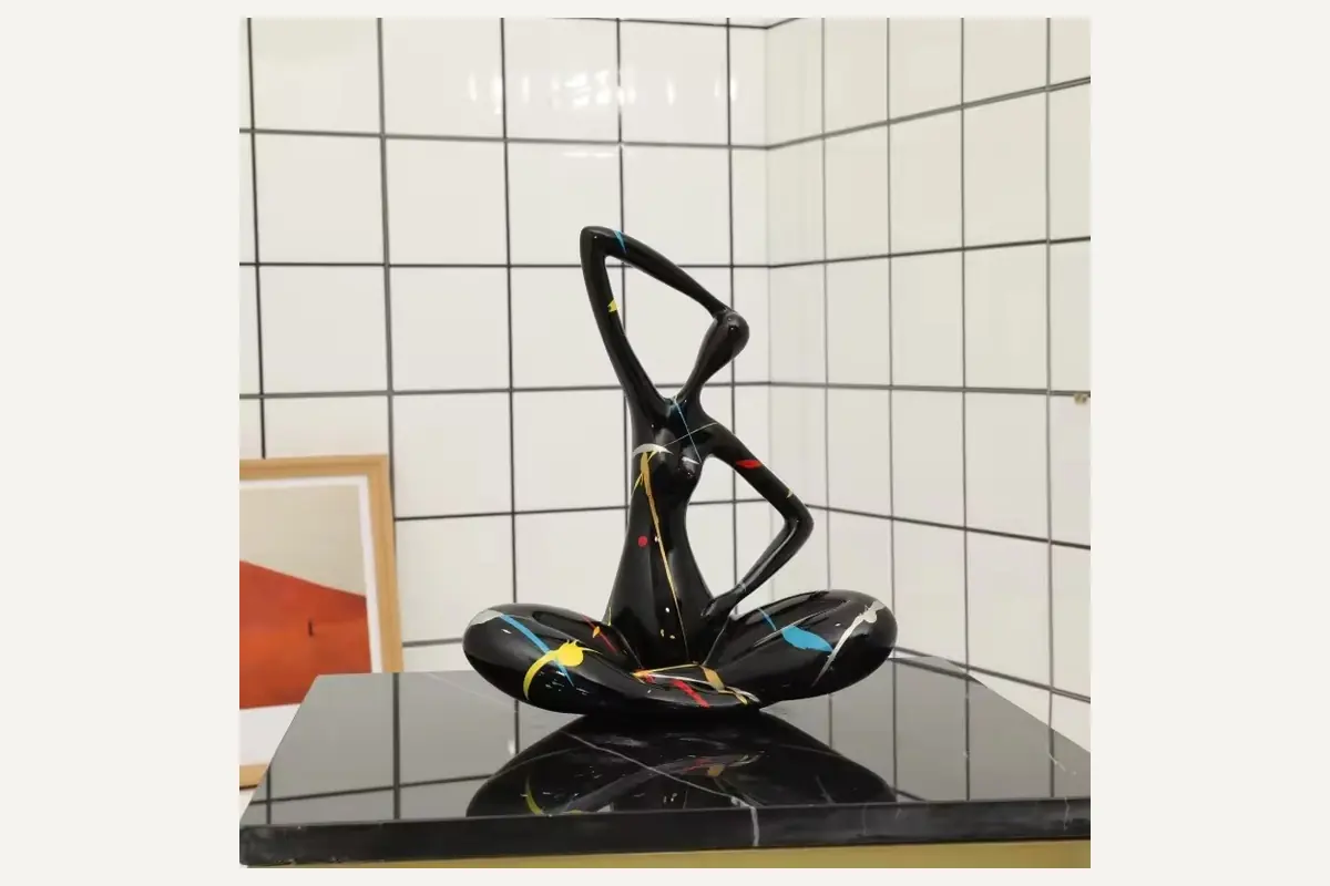 A black abstract woman sculpture in a seated yoga pose with colorful splashes