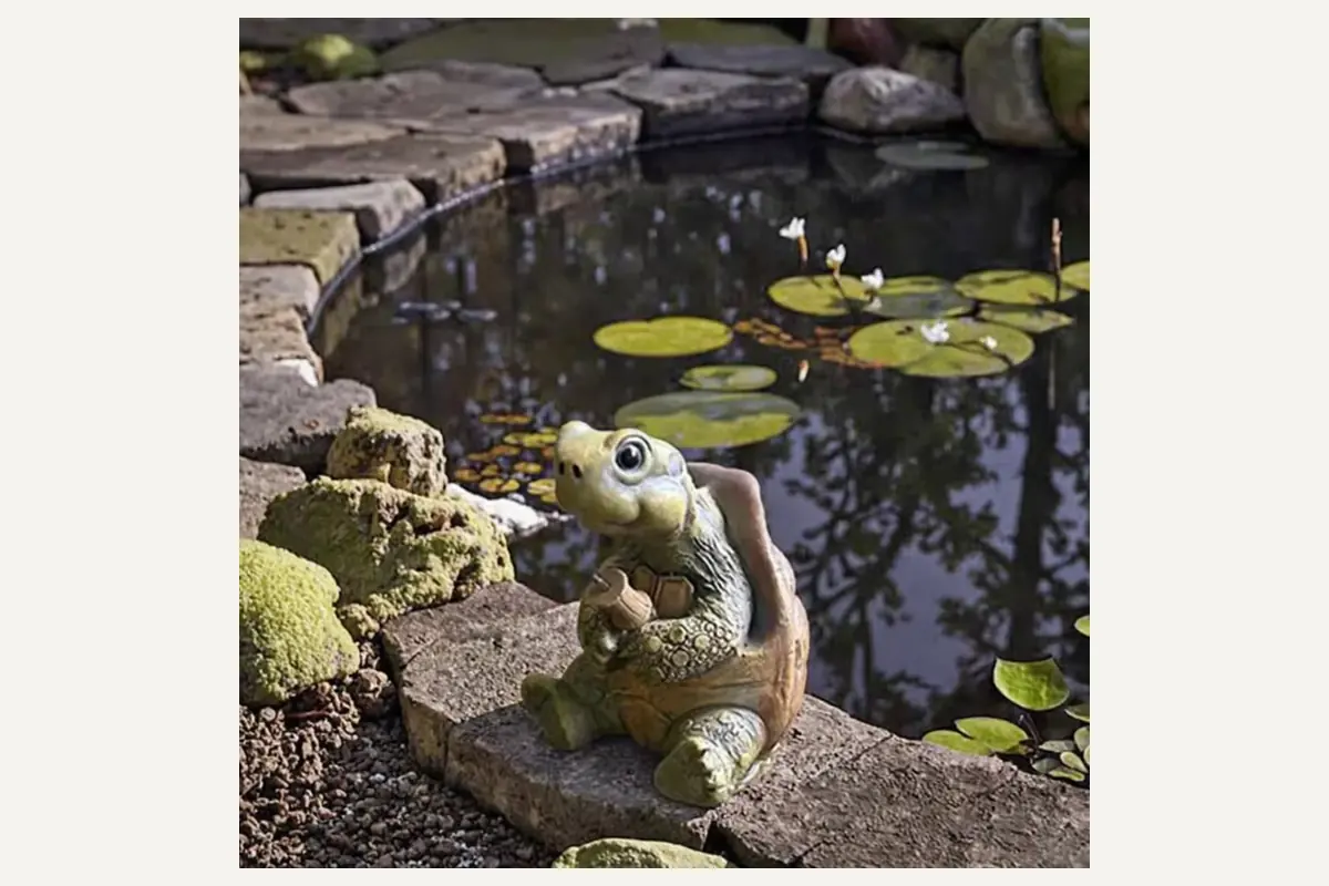 A small turtle garden figurine beside a pond and rocks