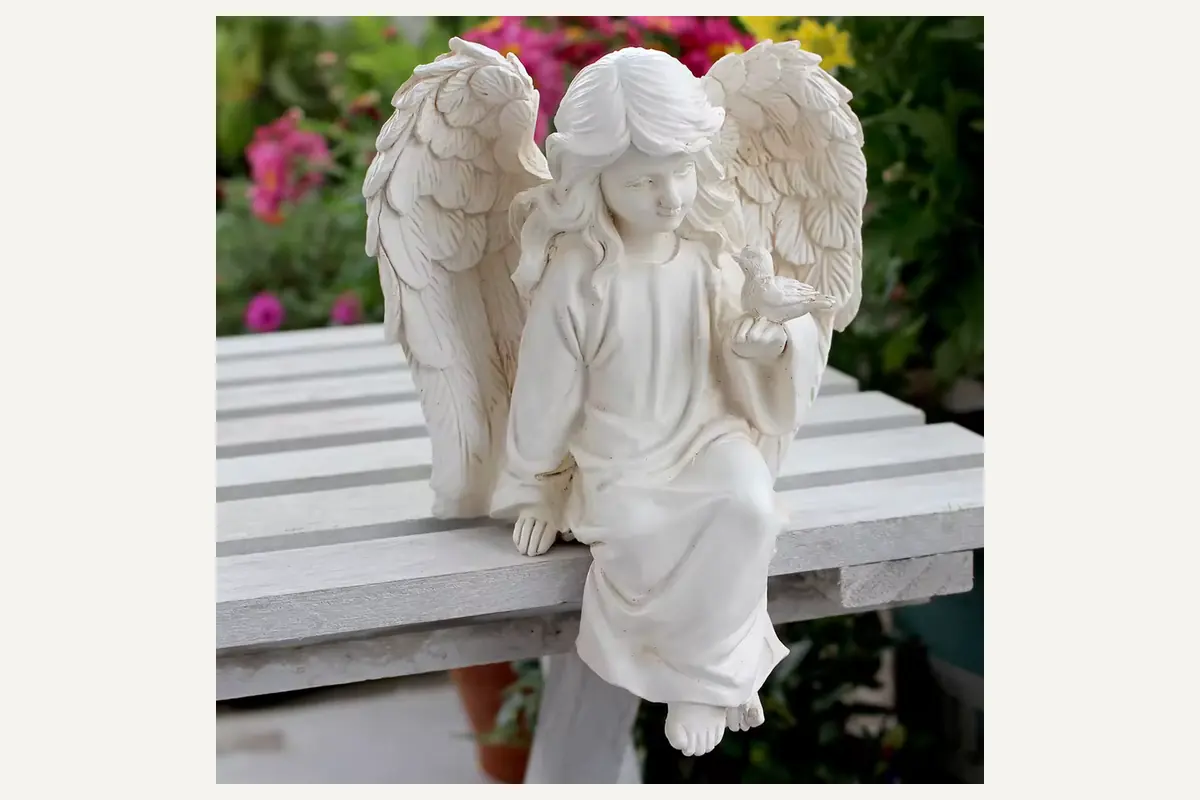 An ivory garden angel sculpture showing draped robes and feathered wings