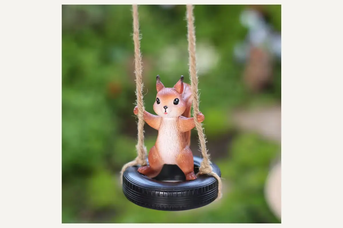 A squirrel-shaped hanging ornament seated on a black tire swing