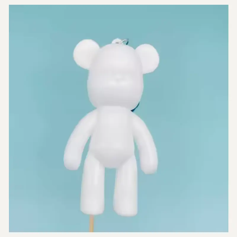 An unpainted block-shaped charm with circular ears, an elongated torso and long straight arms