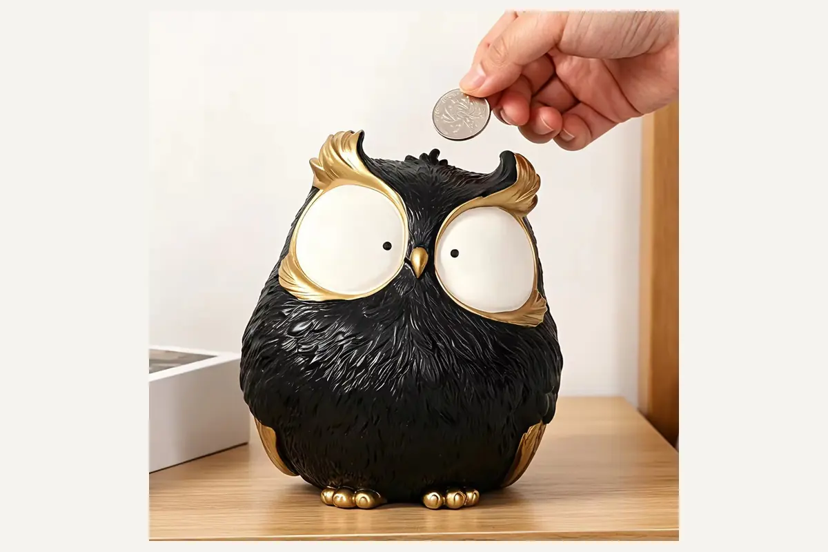 A hand inserting a coin into a black owl-shaped coin bank