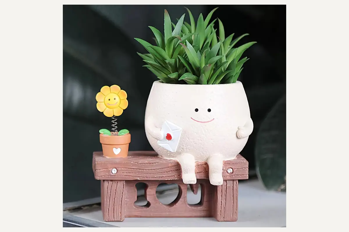 A smiling character planter sitting on a small bench with a succulent