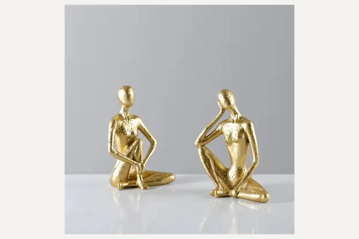 Two gold abstract seated human figurines on a gray surface