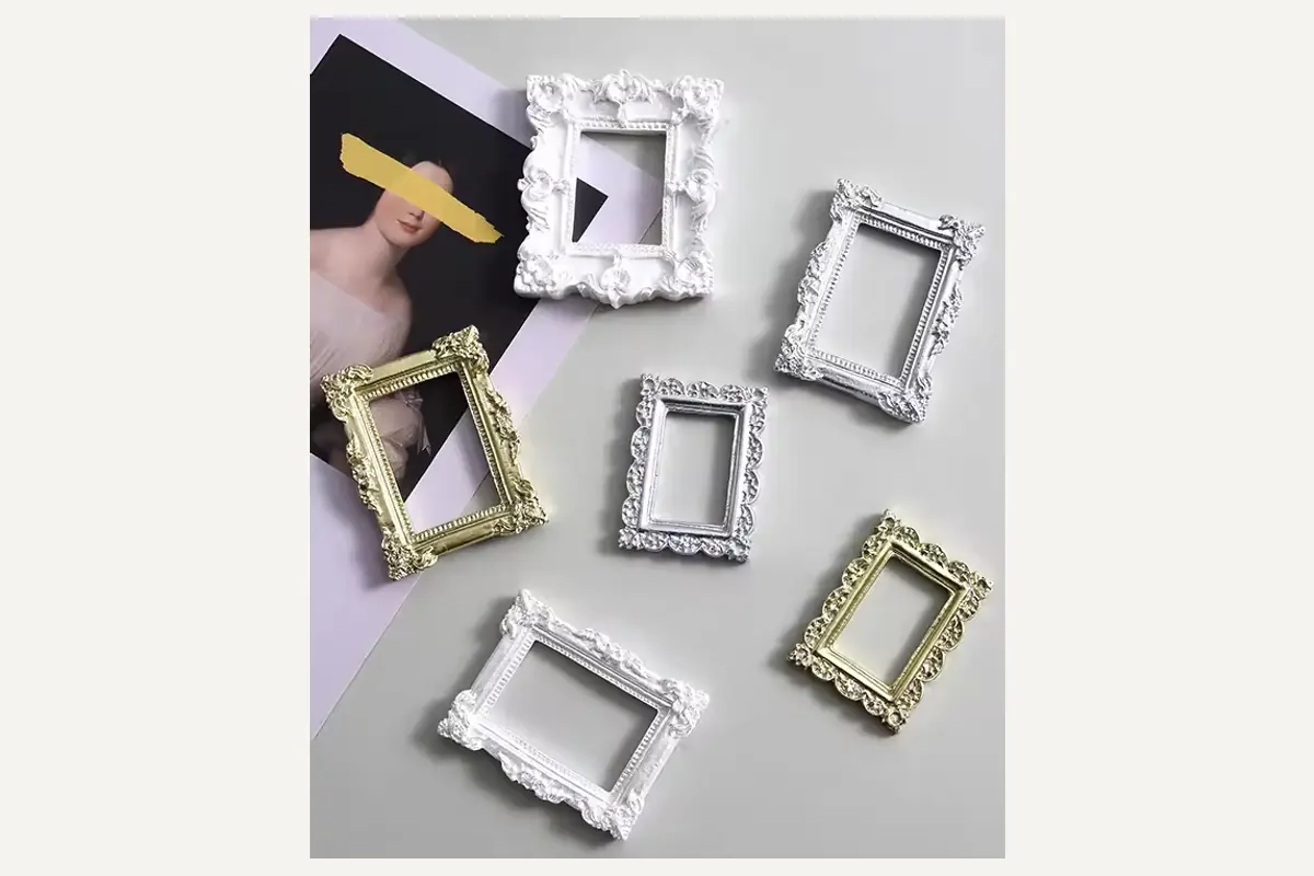 A hand holding a small white ornate picture frame beside frames in several finishes